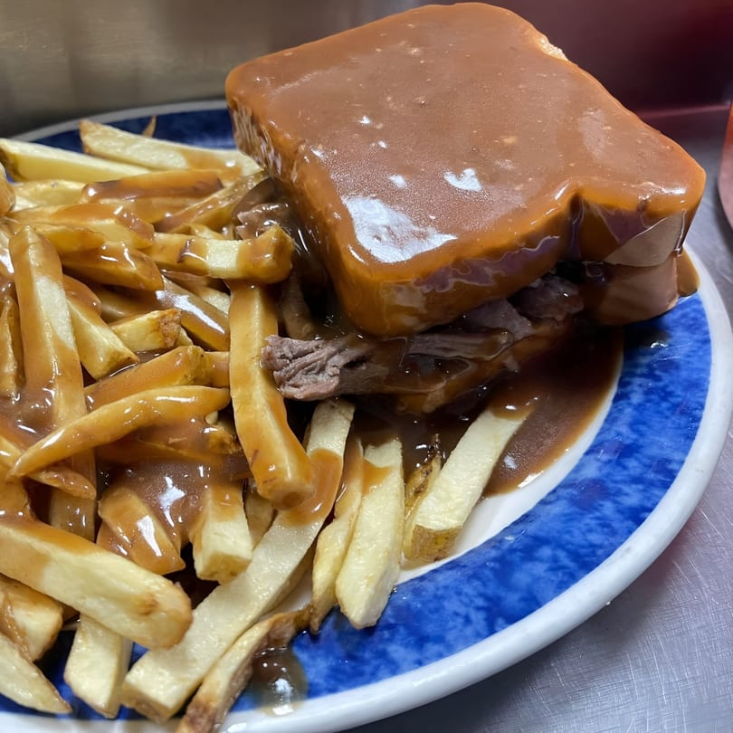 Hot roast beef sandwich with gravy and a side of french fries on a blue and white plate.