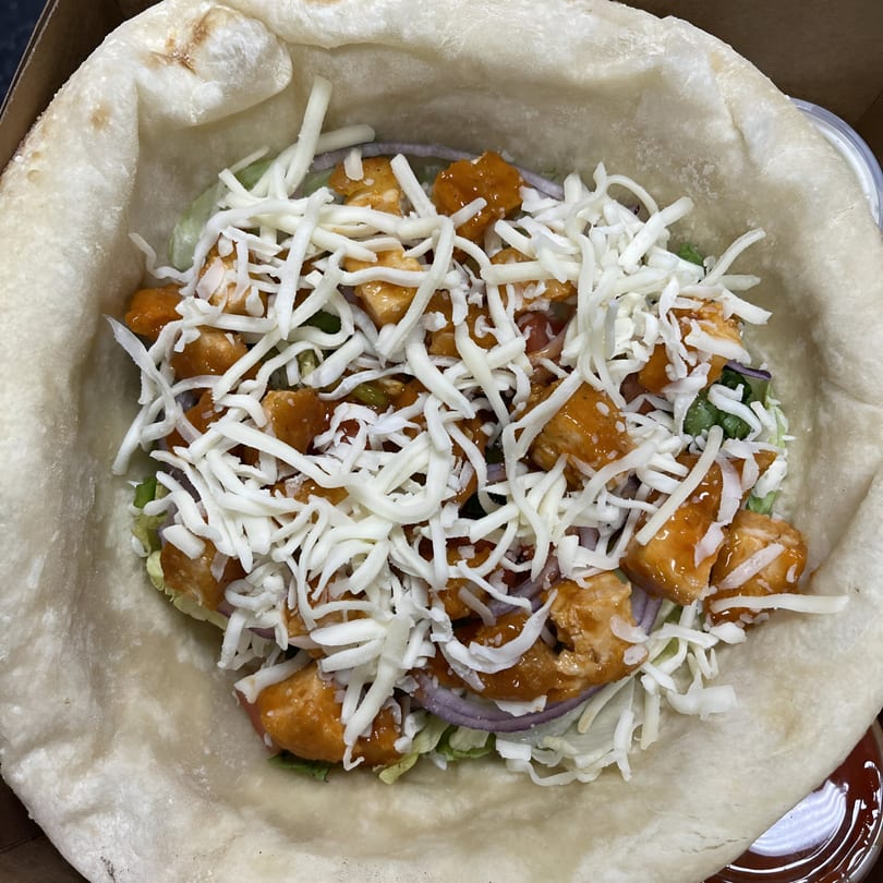 A close-up of a Grandma Bair's chicken wrap with shredded cheese, red onion, and lettuce.