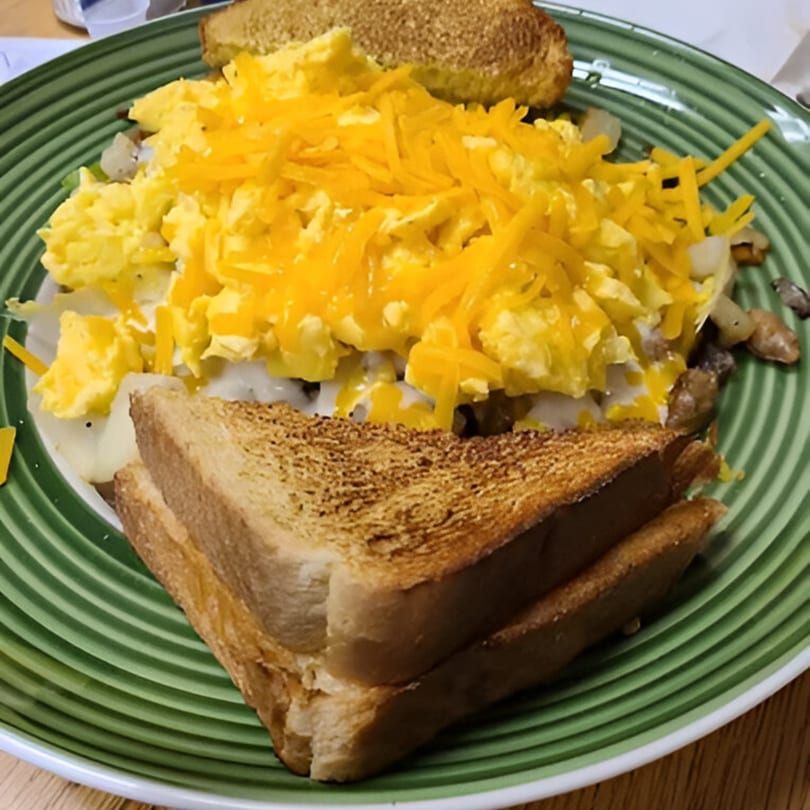 Scrambled eggs with shredded cheese, onions, and toast on a green plate.