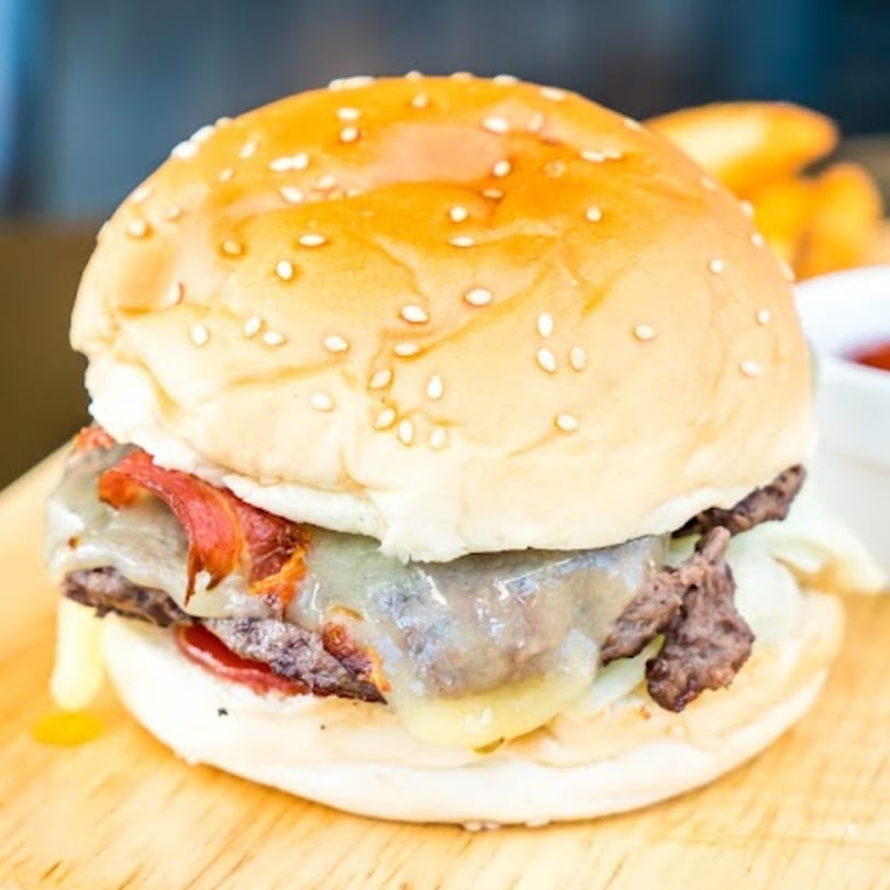 A close-up of a Grandma Bair's bacon cheeseburger with melted cheese and a sesame seed bun.