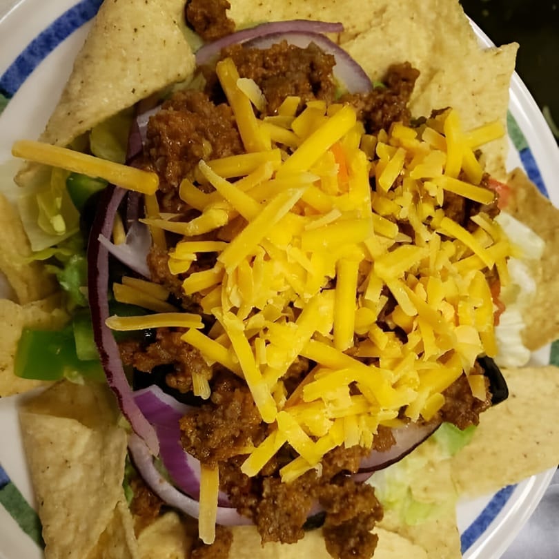 A taco salad with seasoned ground beef, shredded cheddar cheese, red onion, and tortilla chips.